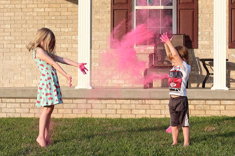 two young children throwing pink colored homemade gender reveal powder in the air outside their home